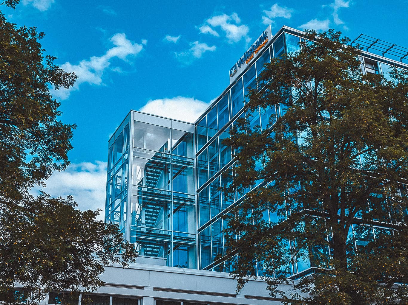 Die Geschäftsstelle der Volksbank Kassel Göttingen am Tag. Zu sehen ist eine Glasfront, davor stehen Bäume.