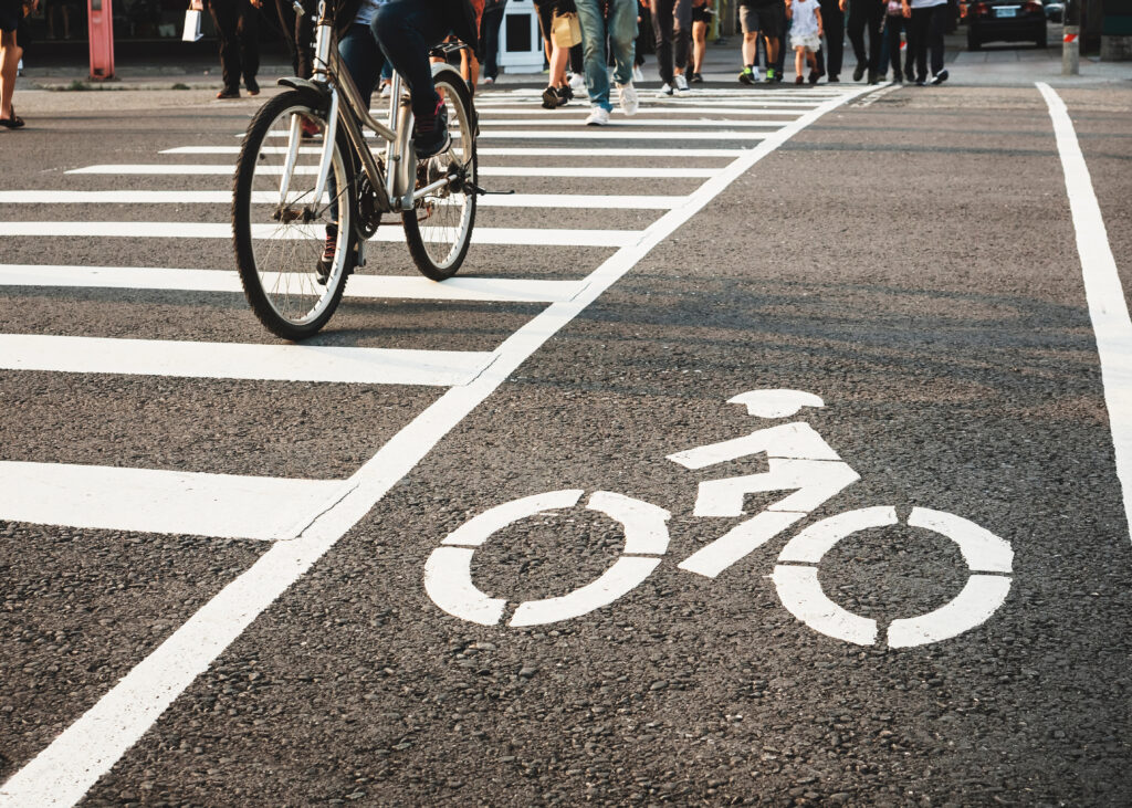 Fahrradweg mit Zebrastreifen, auf dem Menschen mit dem Fahrrad eine städtische Straße überqueren.
