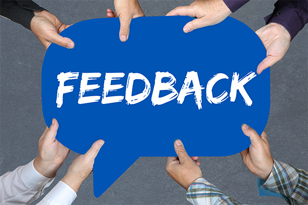 Acht Hände halten eine blaue Sprechblase, auf der in weißer Schrift "Feedback" steht.