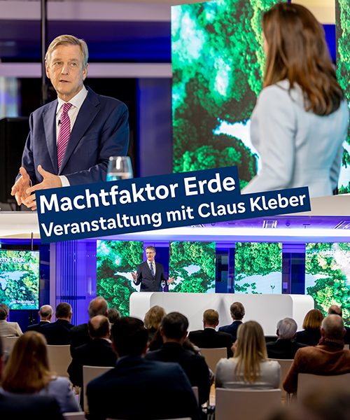 Das Bild ist zweigeteilt und thematisiert die Veranstaltung "Machtfaktor Erde". Im Bild in der oberen Hälfte ist TV-Moderator Claus Kleber im Gespräch mit Veranstaltungsmoderatorin Carina Jantsch zu sehen. Im unteren Bild ist das Podium zu sehen, aufgenommen von der Publikumsseite aus. Deshalb sind im Vordergrund sitzende Menschen von hinten zu sehen. Im Hintergrund ist Vorstandsvorsitzender Wolfgang Osse am Podium zu sehen, der gerade zum Publikum spricht.